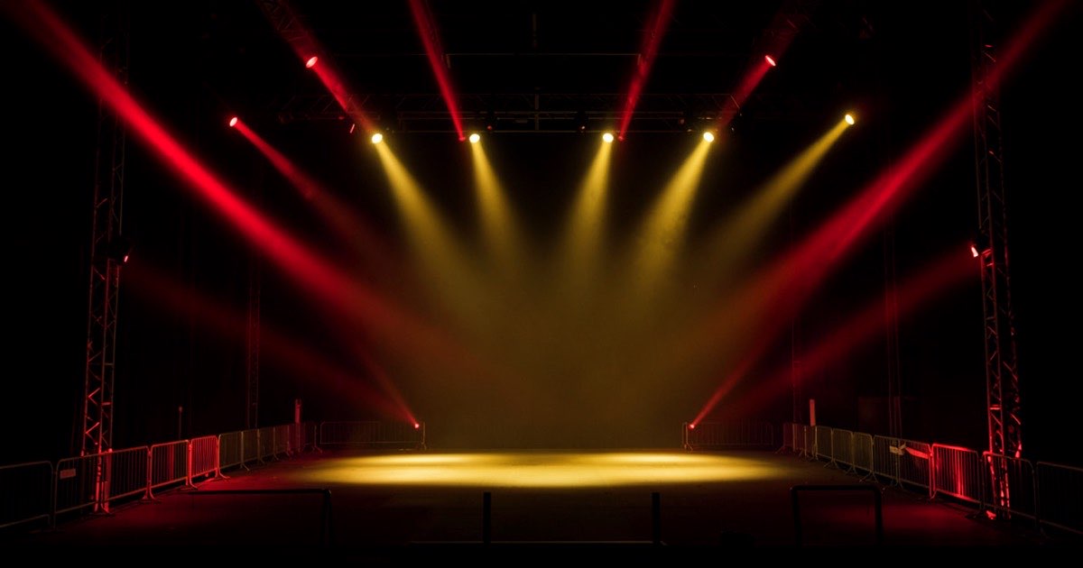 Abstract dark composition of a glowing concert stage surrounded by an overwhelming security perimeter of scanning beams, empty audience area, no people, no text