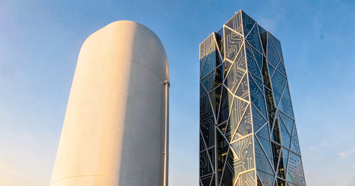 Two abstract corporate towers side by side under a bright blue sky, one with an apple silhouette and one with a circuit board pattern, the apple tower slightly taller.