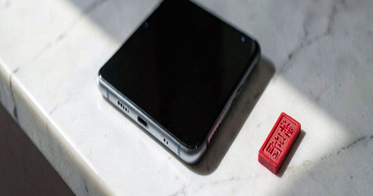 A sleek smartphone on a white marble surface beside a red seal stamp, soft morning light, minimalist editorial still life.