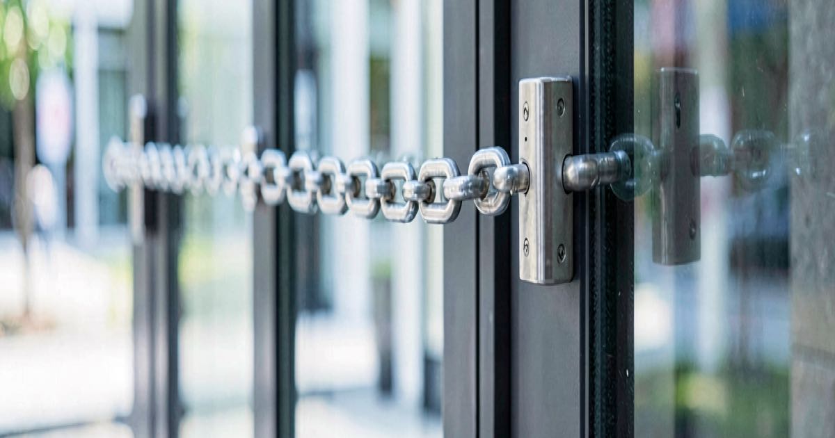 Editorial photograph of a locked glass office building entrance with a chain and padlock, daylight, documentary style, shallow depth of field