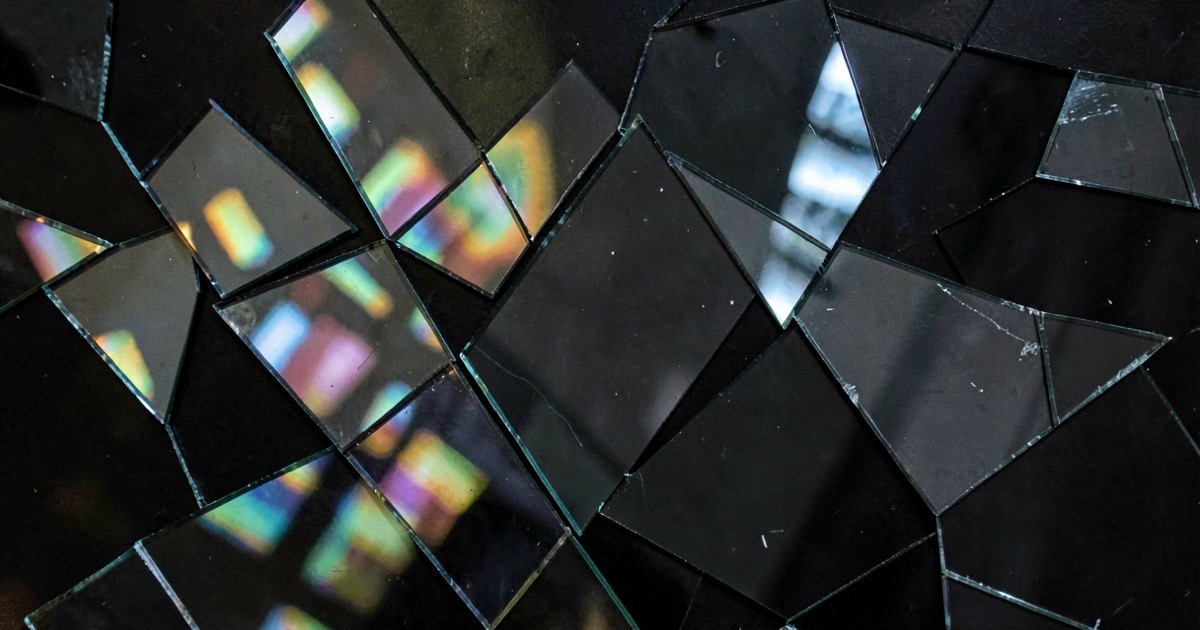 An abstract composition of fragmented mirror pieces reflecting distorted light patterns, suggesting the manipulation of images and identity through AI.