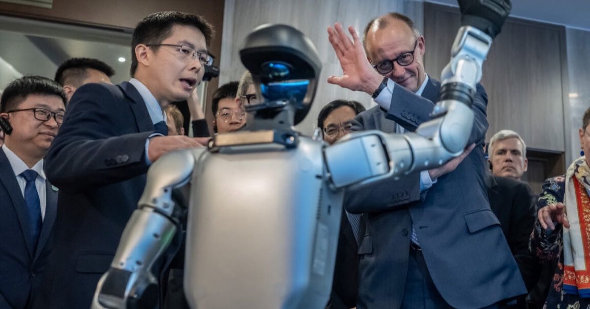 Unitree founder Wang Xingxing demonstrating a Unitree humanoid robot to German Chancellor Friedrich Merz during a visit to Hangzhou, onlookers watching in the background.