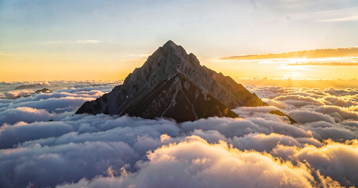 A dramatic mountain peak emerging above a sea of clouds at dawn, symbolising the pursuit of a summit.